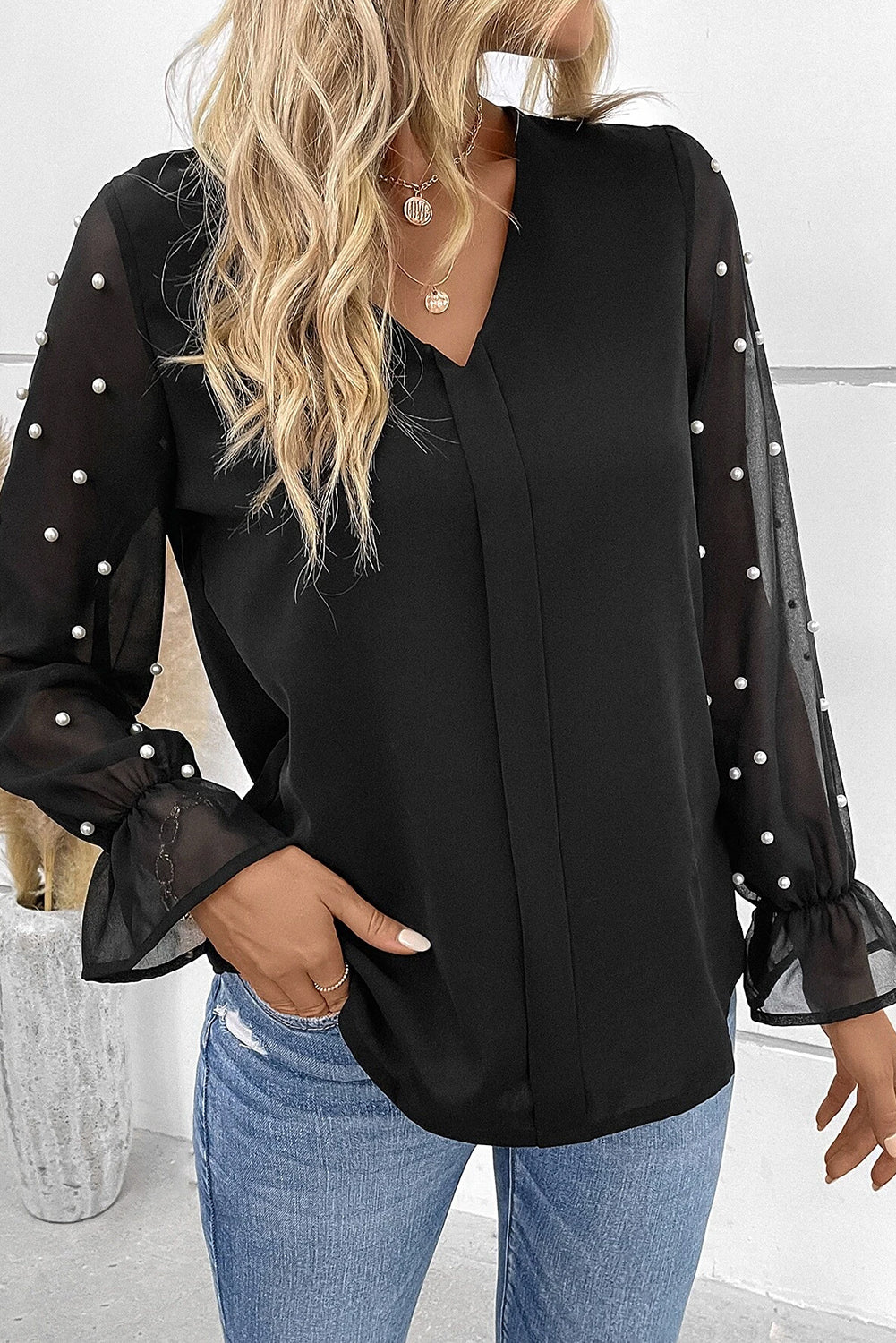 Blouse noire à col en V et manches volantées en maille perlée